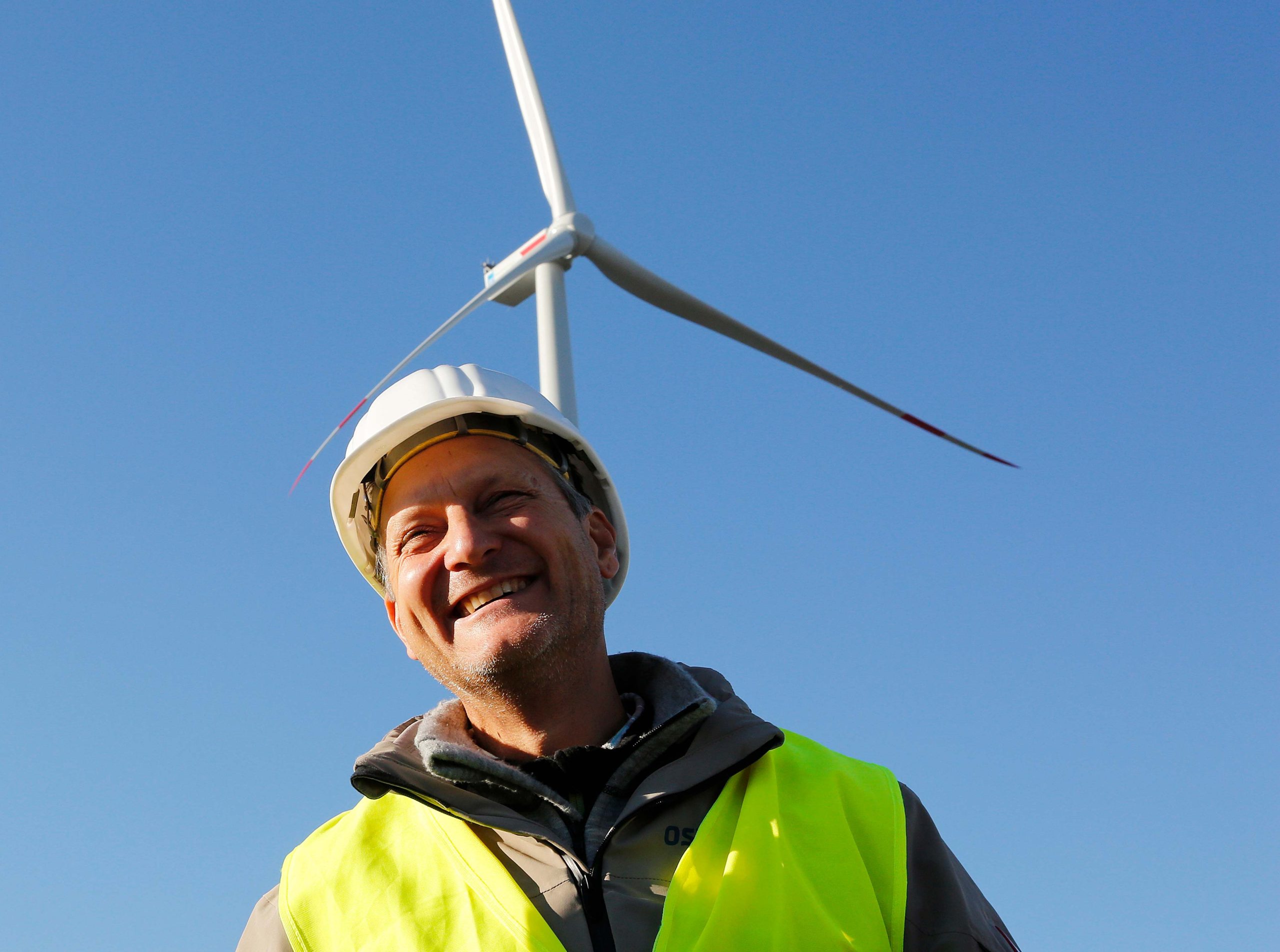 Ein Mitarbeiter von Perigus Energy steht mit Helm und Sicherheitsweste vor einer Windenergieanlage
